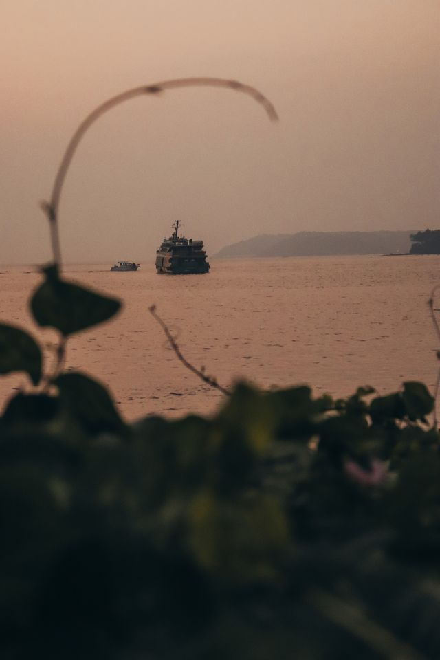 A ship sails peacefully on the ocean at sunset, surrounded by calm waters and coastal scenery.
