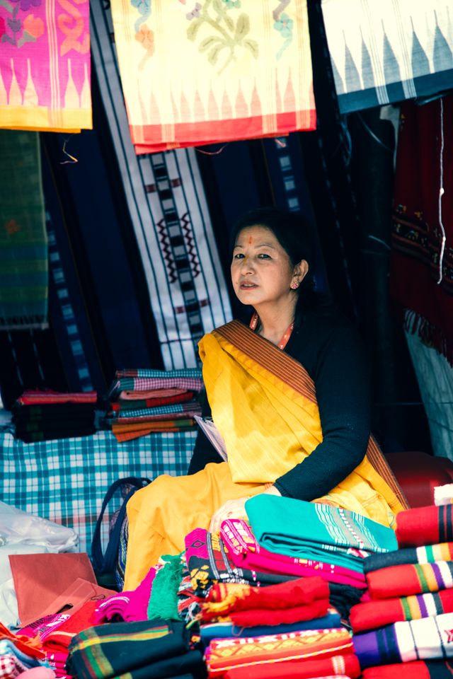 Woman vendor selling colorful textiles at a Delhi market stall.
